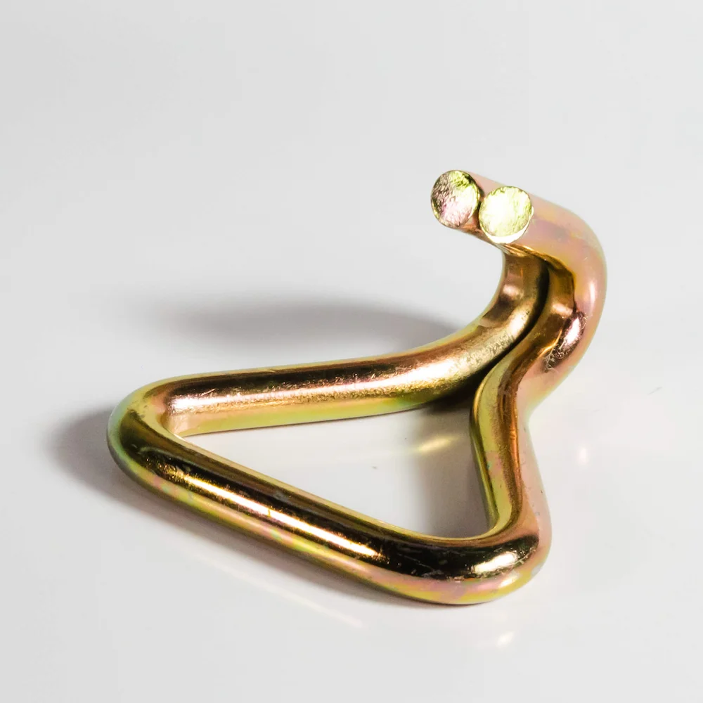 Imagem de um gancho J, dourado, sobre superfície branca.